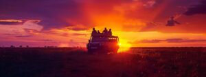 a vibrant sunset illuminates a diverse group of travelers atop an open safari vehicle, surrounded by the breathtaking expanse of tanzania's savanna teeming with wildlife.